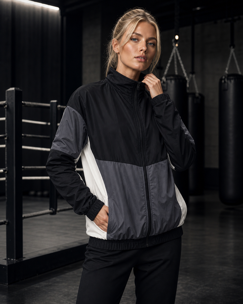 Blonde ATHENIS model wearing the black and grey training windbreaker in a boxing gym